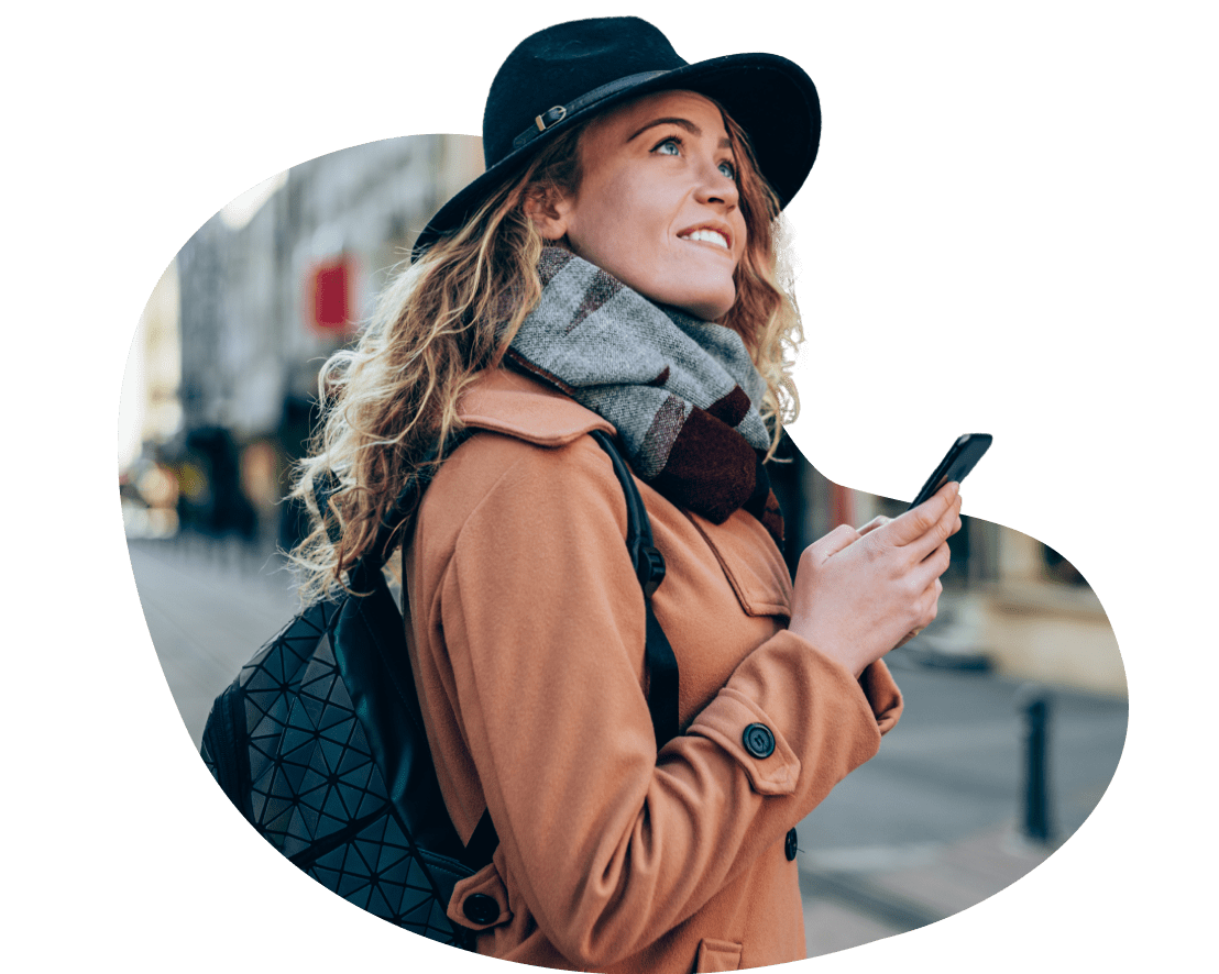 Woman wearing hat and backpack checking her phone while outside.